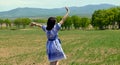 Russian young woman in dress in the Slavic style running and waving her hand to the nature against the background of green field