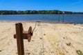 A rusty wench with a long cable in the silky brown sand of the beach on the banks of the rippling lake with lush green treeys