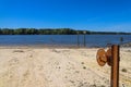 A rusty wench with a long cable in the silky brown sand of the beach on the banks of the rippling lake with lush green trees