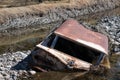Rusted abandoned car half-submerged in water