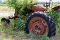 A rusted abandoned old vintage red farm tractor with overgrown wild grass and weeds Royalty Free Stock Photo