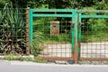 Rusted green metal and wire backyard entrance doors with mounted mailbox surrounded with family house backyard plants and flowers