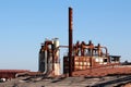 Rusted metal chimneys surrounded with large storage silos on top of destroyed rooftops at abandoned industrial complex