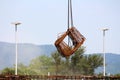 Rusted metal construction frames suspended in air over construction site with strong chain