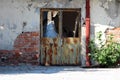 Rusted metal doors with broken glass and without door handle mounted on red brick wall with cracked facade next to broken gutter Royalty Free Stock Photo