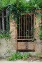 Rusted iron gate in an ancient brick and stone wall overgrown with foliage