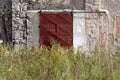 Rusted metal sliding warehouse doors mounted on old dilapidated wall with tall grass and small flowers in front at abandoned Royalty Free Stock Photo