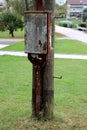 Rusted metal telephone box with metal wire housing mounted on old wooden utility pole surrounded with freshly cut grass