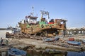 Rusted ship with only a few remains of paint on the iron hull stands in the dry dock in front of the small boats of the fishermen