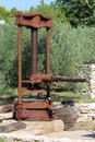 Rusted strong metal vintage olive oil press machine mounted on concrete foundation used as garden decoration with stone wall and Royalty Free Stock Photo