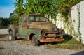 Rusted vintage Chevrolet pickup truck parked by a white fence.