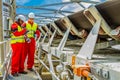 Conveyor belt transporting Platinum ore for processing with mining safety inspectors checking for damage