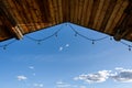 Rustic background of outdoor wood ceiling with log beams and string of lights framing a blue sky with white clouds Royalty Free Stock Photo