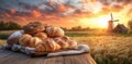 Rustic bread and pastries on wooden table against sunset with windmill and wheat field Royalty Free Stock Photo