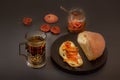 Rustic breakfast with a piece of bread and jam, a glass of hot tea in an antique silver cup holder and a jar of jam on a gray Royalty Free Stock Photo