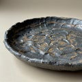 A rustic ceramic plate with a rough, textured surface. The plate features a dark, Royalty Free Stock Photo