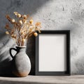 A rustic ceramic vase with dried flowers stands next to a black picture frame on a textured wall casting dramatic Royalty Free Stock Photo
