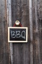 A rustic chalkboard with BBQ written hangs on a wooden wall. Royalty Free Stock Photo