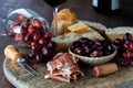 Rustic charcuterie board with bread, prosciutto and olives as well as a tipped wine glass with grapes spilling out.