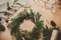 Rustic Christmas wreath. Fir branches, pine cones, thread, berries, cinnamon and golden lights on wooden table. Christmas wreath