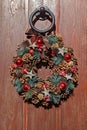 Rustic Christmas wreath hanging on wooden door. Wreath is decorated with natural pine cones, red baubles, and small Royalty Free Stock Photo