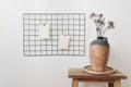 Rustic clay vase with dry hypericum bouquet on wooden table. Black metal mesh noticeboard, bulletin board with blank