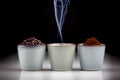 3 rustic coffee cups with coffee grounds, smoking coffee, and ground coffee. Black background