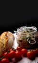 Rustic composition with pate in a jar, red cherry tomatoes and crispy bread on a black background. Royalty Free Stock Photo