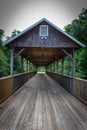 A rustic, covered wooden bridge in a forest.