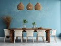 Rustic dining table and white chairs against of blue stucco wall with wooden slab as wall decor. Interior design of dining room Royalty Free Stock Photo