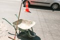 Rustic dirty construction wheelbarrow with push broom on the street, orange road construction cone in the background.