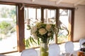 Rustic flower arrangement with white flowers and greenery in a glass vase with water and apples at a wedding banquet. Table set fo