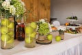 Rustic flower arrangement with white flowers and greenery in a glass vase with water and apples at a wedding banquet. Table set fo Royalty Free Stock Photo