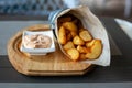 Rustic Fried potato wedges in a paper envelope with sauce on a wooden plate on the outdoor terrace in a cafe Royalty Free Stock Photo
