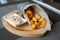 Rustic Fried potato wedges in a paper envelope with sauce on a wooden plate on the outdoor terrace in a cafe Royalty Free Stock Photo