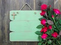 Rustic green blank sign with wooden cross and flower border of red roses hanging on wood door Royalty Free Stock Photo