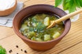 Rustic green soup with vegetables in a clay plate on a wooden background