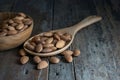 On a rustic hardwood floor, almonds in a wooden ladle and a wooden bowl