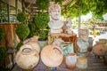 Rustic head planters, flower pots and amphora under shaded area sitting on wood with garden center in bright sun in background