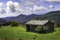 Rustic high mountain cottage in green landscape with clouds and blue sky