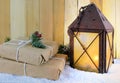 A rustic lantern with a glowing candle inside on a wooden table with hand-wrapped gifts in brown paper for Christmas in December.