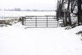 Rustic metal gate and fence locked by the entrance of a vast snow covered farm field in winter Royalty Free Stock Photo