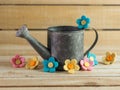 Rustic metal gray watering can surrounded by pink, blue and yellow felt flowers on a natural wood background, perfect home decor Royalty Free Stock Photo