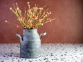 Rustic metal milk can filled with orange artificial flower buds on a terrazzo counter with a terra-cotta background. Country Royalty Free Stock Photo