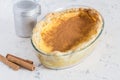 Rustic milk tart on kitchen surface with cinnamon sticks and cinnamon sprinkler