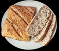 Rustic Multigrain Bread Sliced Loaf on White Ceramic Platter Isolated on Black Background