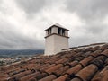 Rustic outdoor fireplace and roof under cloudy gray skies. White work roof chimney. Old tiles on roof with chimney pipe. Red tile