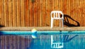 Rustic pool side space outskirts villa back yard white plastic chair and ball float water surface background view fenced by wooden