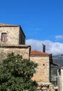 Rustic rock building in seaside Greek village with terra cotta roof tiles and a metal bird fastened onto the metal stove pipe - Royalty Free Stock Photo