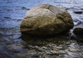 Rustic round boulder, reflections and curvy waves on the sea water Royalty Free Stock Photo